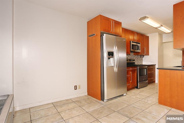 kitchen featuring light tile patterned floors, backsplash, stainless steel appliances, and dark countertops