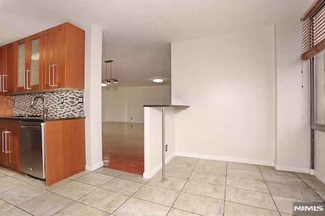 kitchen featuring dark countertops, a sink, light tile patterned flooring, and stainless steel dishwasher