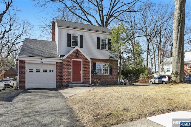 view of front of home with driveway, a front yard, an attached garage, brick siding, and a chimney