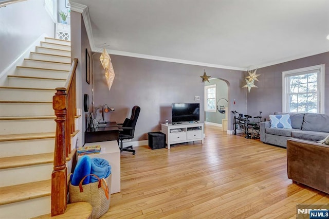 living room with arched walkways, stairway, crown molding, and light wood-type flooring