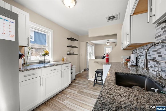 kitchen with visible vents, stone countertops, a sink, white cabinetry, and decorative backsplash