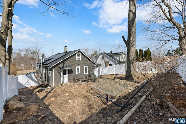 rear view of house featuring roof mounted solar panels, a chimney, a fenced backyard, and a gate