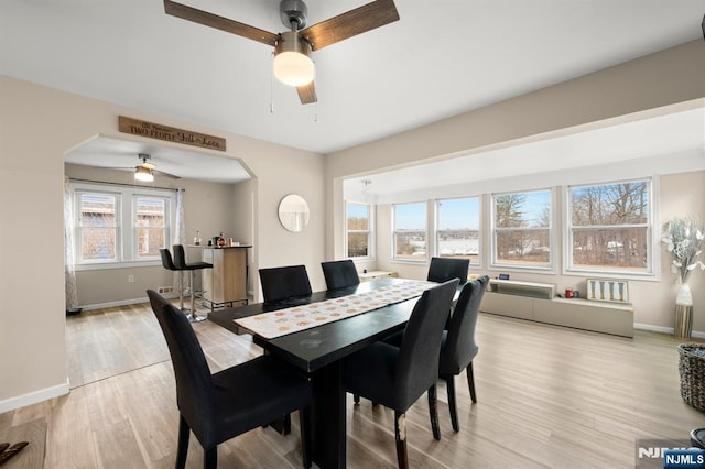 dining space featuring baseboards, arched walkways, a ceiling fan, and light wood finished floors