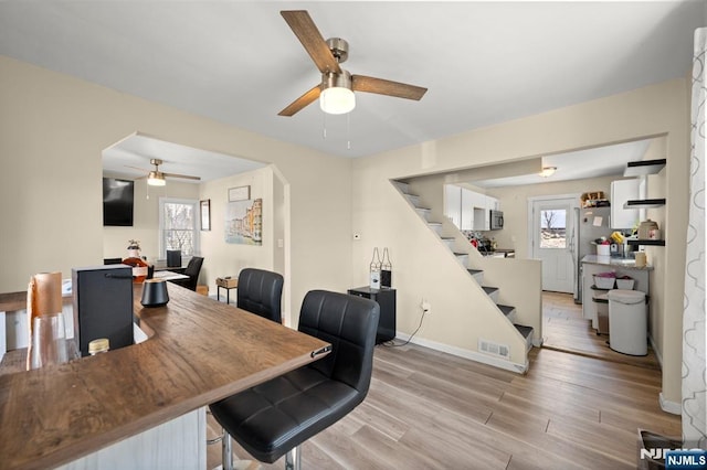 dining area featuring light wood finished floors, baseboards, ceiling fan, stairs, and arched walkways