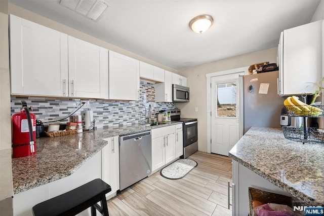 kitchen with a sink, light stone counters, appliances with stainless steel finishes, white cabinets, and decorative backsplash