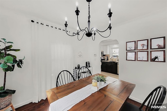 dining room featuring a notable chandelier, wood finished floors, arched walkways, crown molding, and baseboards