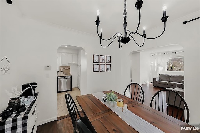 dining room with wood finished floors, arched walkways, a chandelier, and ornamental molding