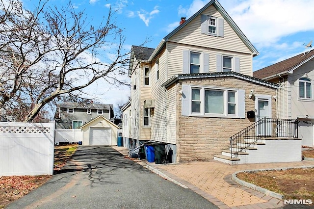 view of front of property with fence, aphalt driveway, a garage, an outdoor structure, and stone siding