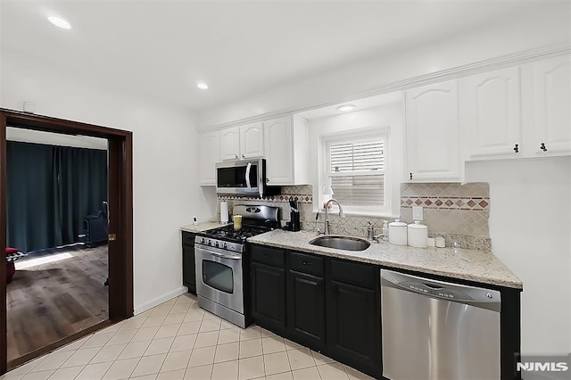 kitchen with white cabinetry, appliances with stainless steel finishes, light stone countertops, and a sink