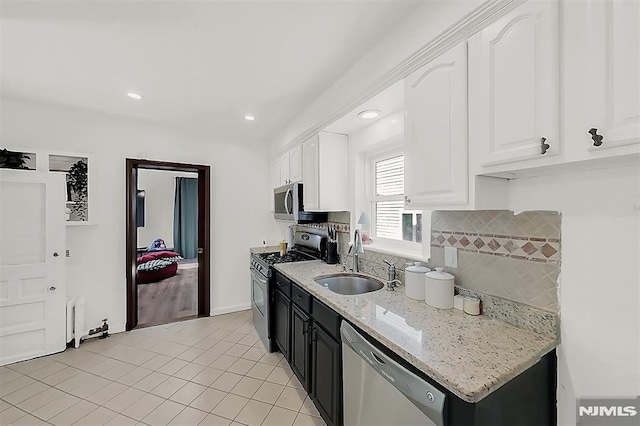 kitchen with light stone counters, a sink, stainless steel appliances, white cabinets, and tasteful backsplash