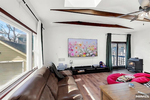 living area featuring a ceiling fan, lofted ceiling with beams, a wood stove, and wood finished floors