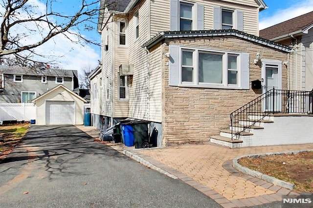 view of side of property with stone siding, driveway, a detached garage, and an outdoor structure