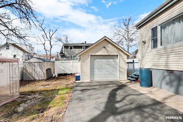 detached garage featuring driveway and fence