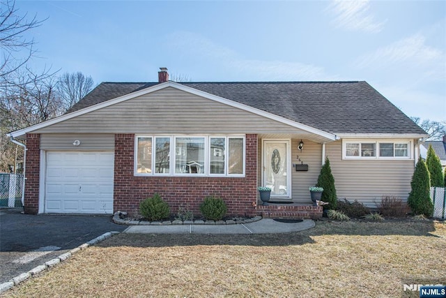 view of front facade with a front yard, roof with shingles, an attached garage, a chimney, and brick siding