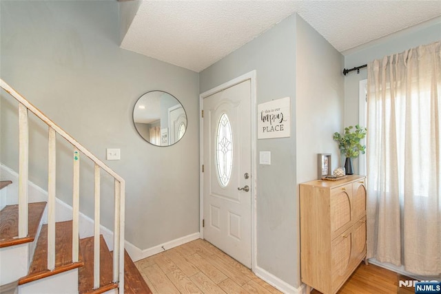 entryway featuring stairway, baseboards, light wood finished floors, and a textured ceiling