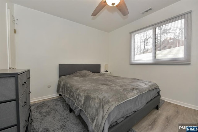 bedroom featuring ceiling fan, visible vents, baseboards, and wood finished floors