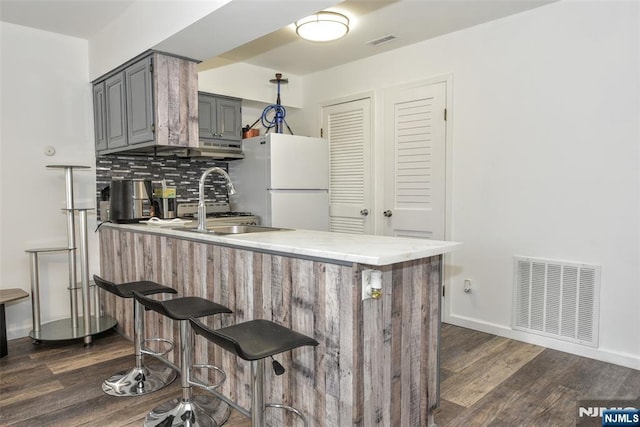 kitchen featuring visible vents, a peninsula, gray cabinets, and freestanding refrigerator