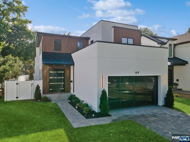 view of front of property featuring stucco siding, a gate, a front yard, an attached garage, and metal roof