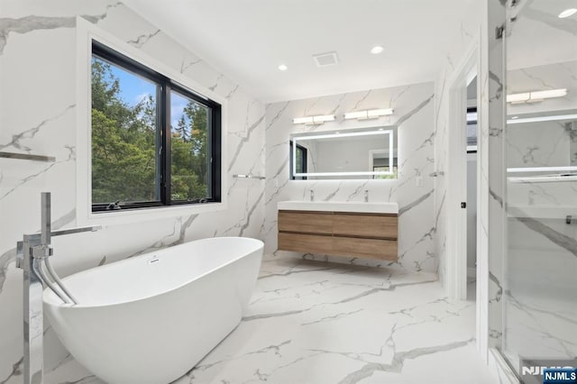 bathroom with vanity, stone wall, a soaking tub, recessed lighting, and marble finish floor