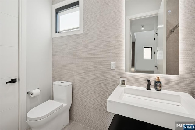 bathroom featuring tile walls, toilet, and a sink