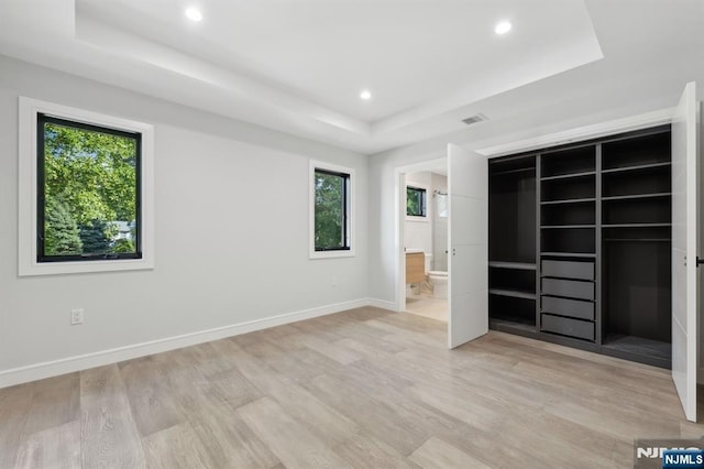 unfurnished bedroom featuring visible vents, baseboards, light wood-type flooring, a tray ceiling, and recessed lighting