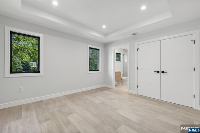 unfurnished bedroom with baseboards, visible vents, light wood-style flooring, recessed lighting, and a raised ceiling