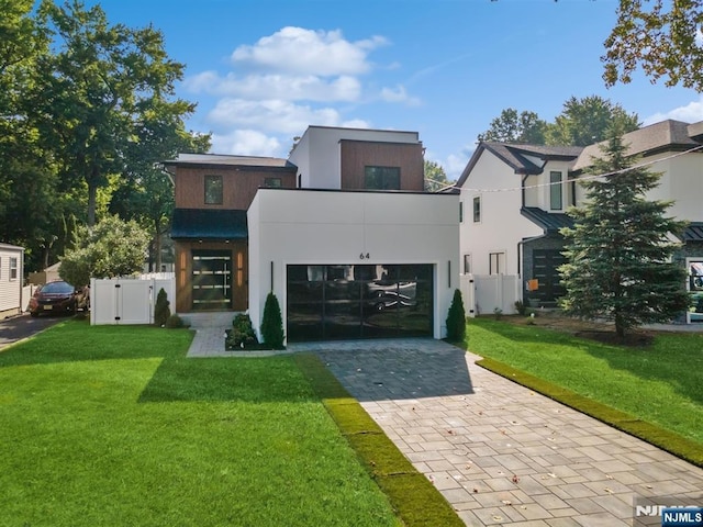 modern home with a front lawn, fence, stucco siding, decorative driveway, and a garage