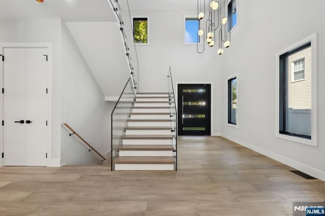 foyer with wood finished floors, visible vents, a towering ceiling, and baseboards