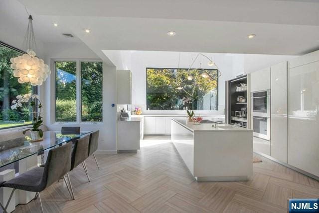 kitchen with decorative light fixtures, an island with sink, light countertops, white cabinets, and modern cabinets