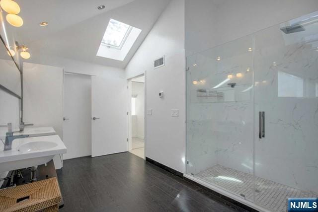 bathroom with a sink, wood finished floors, a marble finish shower, double vanity, and lofted ceiling