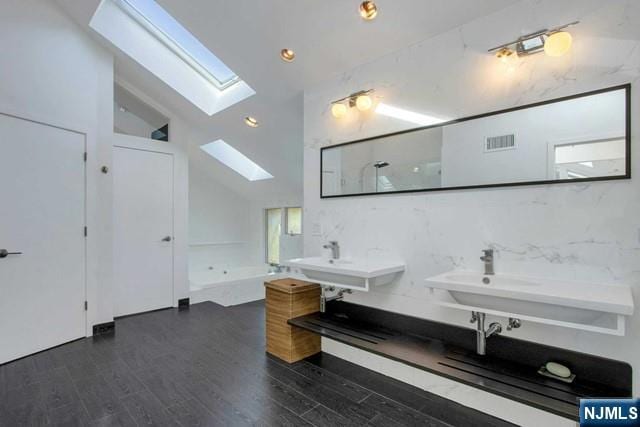 full bath featuring wood finished floors, a bathing tub, visible vents, two sinks, and a skylight