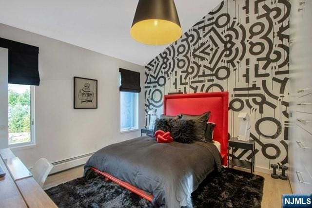 bedroom with a baseboard radiator, an accent wall, and wood finished floors