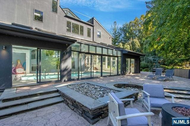 rear view of house featuring a patio area, stucco siding, and an outdoor fire pit