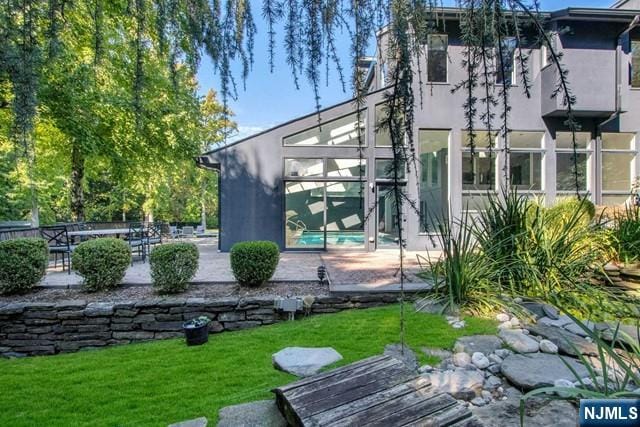 rear view of house with stucco siding, a patio, glass enclosure, a yard, and an outdoor pool