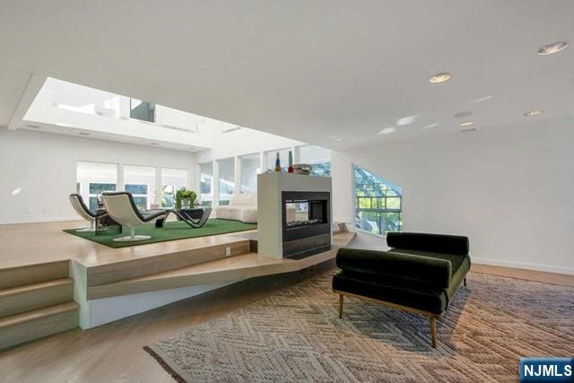 living area with recessed lighting, wood finished floors, a multi sided fireplace, and baseboards