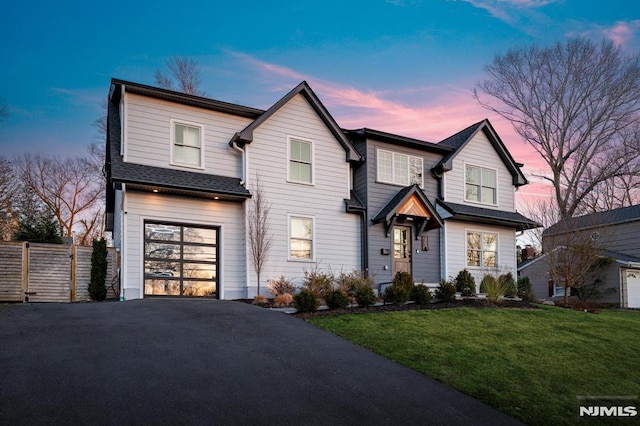 view of front of home featuring a shingled roof, fence, aphalt driveway, a lawn, and a garage