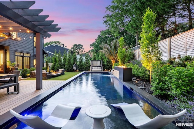 pool at dusk featuring a fenced backyard, a pergola, and a wooden deck