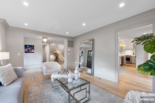 living room with visible vents, light wood-style flooring, ornamental molding, recessed lighting, and stairway