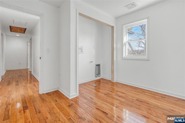 corridor with visible vents, baseboards, heating unit, and light wood-style flooring