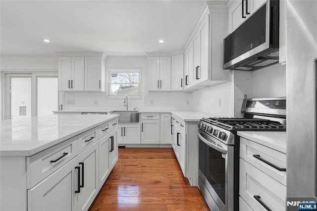 kitchen with wood finished floors, recessed lighting, a sink, stainless steel appliances, and white cabinetry