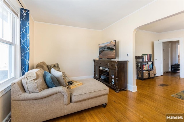 living room featuring arched walkways, light wood finished floors, crown molding, and baseboards