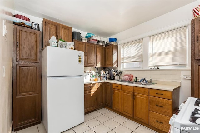 kitchen featuring range with gas stovetop, freestanding refrigerator, a sink, decorative backsplash, and light countertops