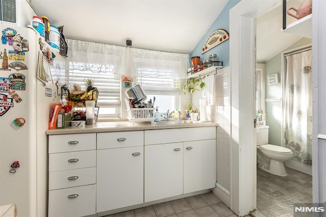 bathroom featuring toilet, vanity, vaulted ceiling, tile patterned floors, and tile walls