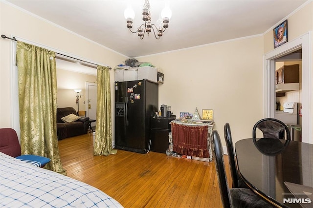 bedroom with a notable chandelier, ornamental molding, wood finished floors, and black refrigerator with ice dispenser