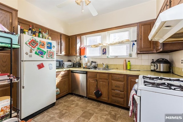 kitchen featuring under cabinet range hood, light countertops, brown cabinets, white appliances, and a sink