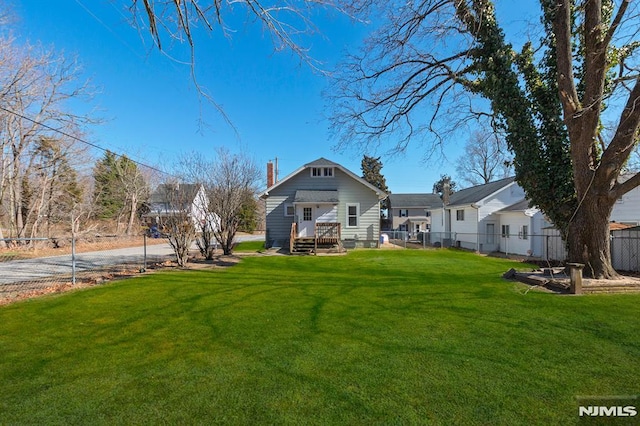 rear view of house with entry steps, a lawn, fence, and a chimney