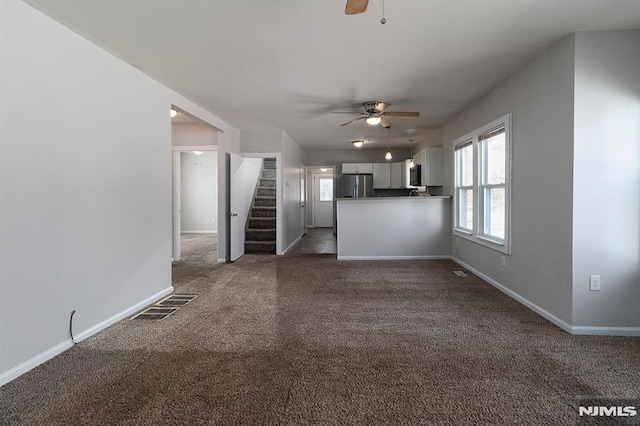 unfurnished living room featuring visible vents, a ceiling fan, stairway, carpet, and baseboards