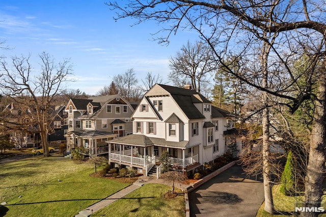 back of house with a porch, a gambrel roof, aphalt driveway, a lawn, and a residential view