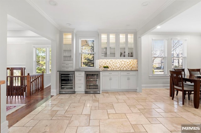 bar featuring beverage cooler, backsplash, crown molding, and baseboards