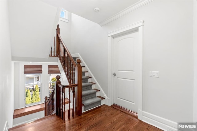 staircase featuring ornamental molding, wood finished floors, baseboards, and a healthy amount of sunlight